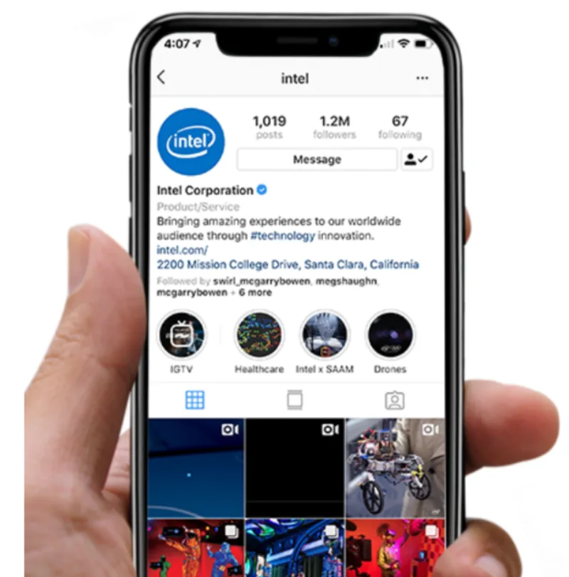 A hand holding a smartphone displaying the Intel Corporation's Instagram profile, showcasing their posts, follower count, and navigation icons.
